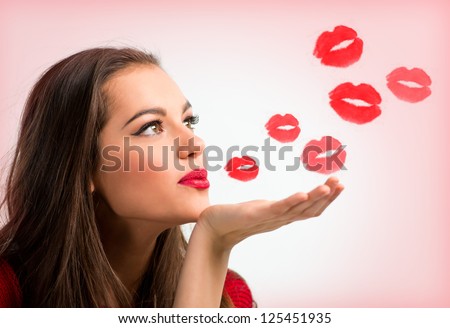 Portrait of a beautiful woman blowing  red kisses over a pink background