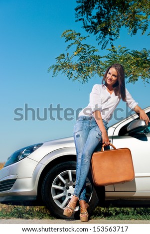Beautiful woman with suitcase leaning on a car