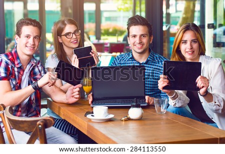 Group of young people sitting at a cafe, holding electronic gadgets