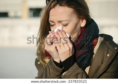 Young woman sneezes and running nose during cold day and holding tissue next to her nose