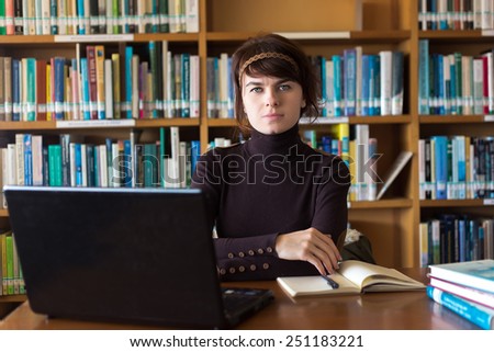 Student girl sitting with books and laptop computer in college library. Exemplary student. Selective focus on face.