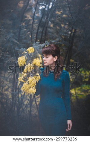 Beautiful young woman with yellow mimosa flowers. Art processing with color grading and shallow depth of field and soft focus.