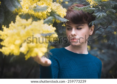 Beautiful young woman with yellow mimosa flowers. Art processing with color grading and shallow depth of field. Selective focus on face.