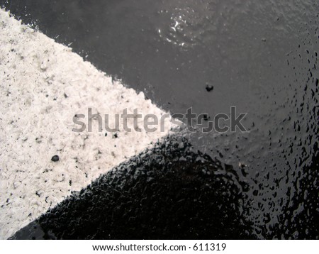 The point of a white arrow on wet pavement with rain.