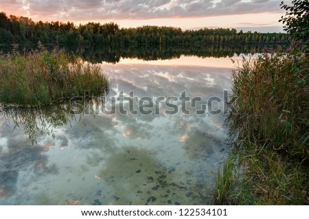 Sunset over Svetloyar Lake with forest along bank reflecting in calm water