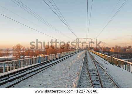 Straight snow-bound railroad on bridge vanishing in horizon with power line along against skyline background. Moscow, Russia.