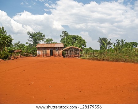 Brick house and other building with plain ground field before  against plants and cloudy sky background. Jinja, Uganda, Africa.