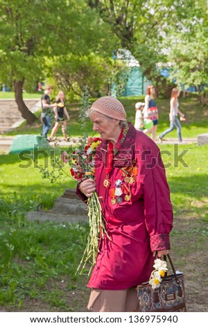 MOSCOW/RUSSIA - MAY 9: Old woman veteran of WWII with bag and bunch of flowers walks during festivities devoted to 65th anniversary of Victory Day on May 9, 2010 in Moscow.