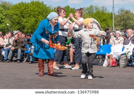 MOSCOW/RUSSIA - MAY 9: Old woman veteran of WWII in blue coat with awards dances with little girl among other children in festivities devoted to anniversary of Victory Day on May 9, 2011 in Moscow.