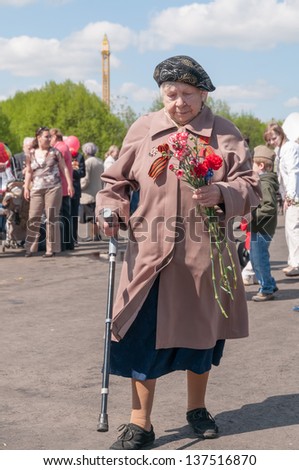 MOSCOW/RUSSIA - MAY 9: Old woman veteran of WWII with walkingstick and bunch of flowers walks during festivities devoted to 65th anniversary of Victory Day on May 9, 2011 in Moscow.