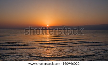 Bright sunrise over Jordan mountain Dead Sea shore with sun ray reflection on wavy water surface. Metzoke Dragot, Israel.