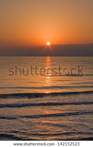 Sunrise over Jordan mountain Dead Sea shore with bright sun ray reflection on wavy water surface. Metzoke Dragot, Israel.