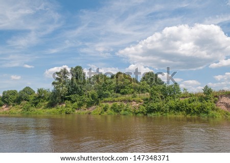 View on steep river bank with trees and bush growth on riverside against blue sky background. Kaluzhsky region, Russia.