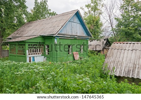 Old abandoned green wooden house with porch and broken windows among wild tall weeds. Bolshaya Doroga village, Tambovsky region, Russia.