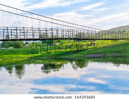 Old lengthy hanging wooden footbridge with rails over river. Arkhangelsky region, Russia.