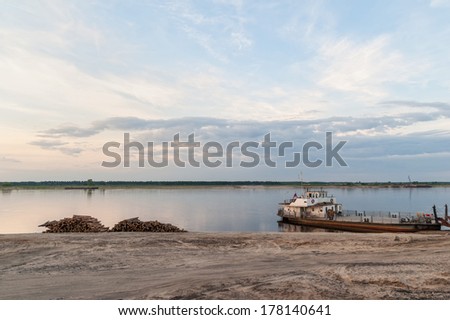 Timber store sinks in water along riverside and ferry against panorama of Severnaya Dvina river at sunset .