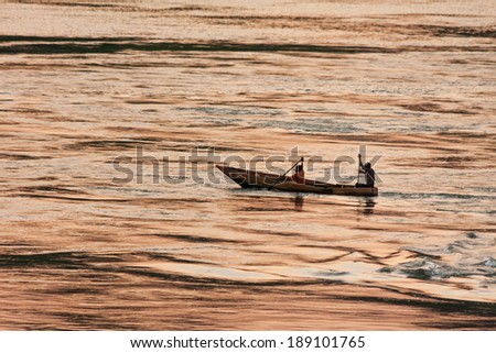 Fishers in boat rows against evening glow reflection in Victoria Nile River background at sunset. Jinja, Uganda, Eastern Africa.