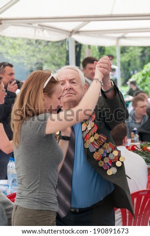 MOSCOW/RUSSIA - MAY 9: Old man veteran of WWII decorated with numerous orders and medals dances with young woman in Gorky Park during festivities devoted to Victory Day on May 9, 2013 in Moscow.