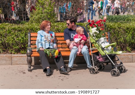 MOSCOW/RUSSIA - MAY 9: Old woman WWII veteran decorated with numerous orders and medals and man holding kid on knees sit on bench during festivities devoted to Victory Day on May 9, 2013 in Moscow.