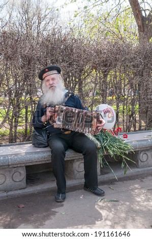 MOSCOW/RUSSIA - MAY 9: Old grey-haired bearded accordion player in vintage navy uniform decorated with medals sits on bench during festivities devoted to Victory Day on May 9, 2013 in Moscow.