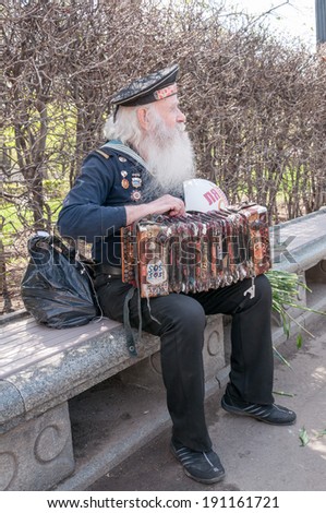 MOSCOW/RUSSIA - MAY 9: Old grey-haired bearded accordion player in vintage navy uniform decorated with medals sits on bench during festivities devoted to Victory Day on May 9, 2013 in Moscow.