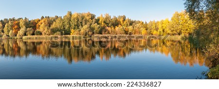 Panoramic view on lake with forest reflecting in calm water in Indian summer. Moscow, Russia.