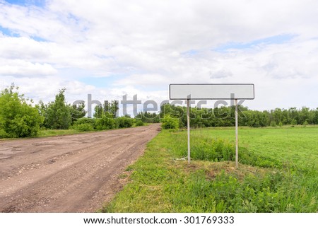 Straight dirty road with white empty sign on roadside at entrance to town. Bolshaya Doroga village, Tambovsky region, Russia.