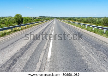 Vanishing straight highway with metal rails along. Kozelsk, Kaluzhsky region, Russia.