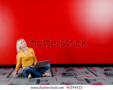 young blond sitting on the floor with the laptop on her knees in front of the red wall