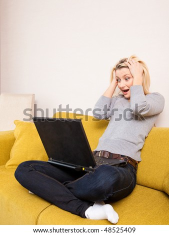 surprised young blond woman sitting on couch and looking at computer