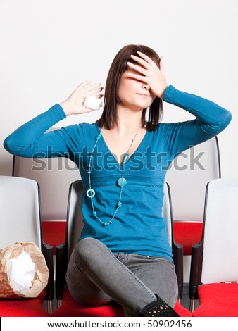 scared young woman sitting and covering her eyes with hand while watching movie, holding tissue, vertical shot