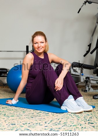 A young woman sitting on stretching carpet in a health club. Vertical shot.