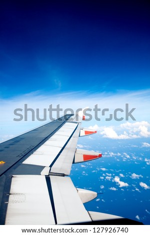 View from window seat of an airplane overlooking blue sky and clouds.