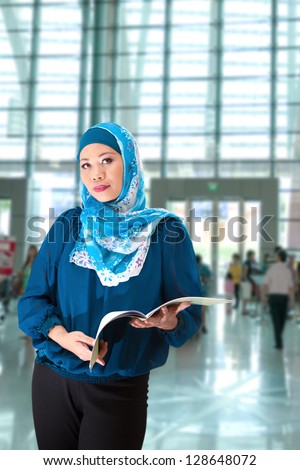 A mature Muslim woman with a book in exhibition hall