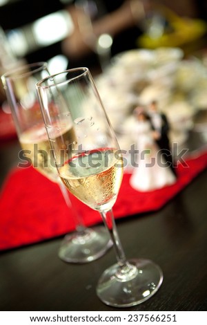 Two glasses of champagne on table with bride and groom plastic figure in background showing a wedding event.