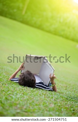 Young boy lying on open park reading a book