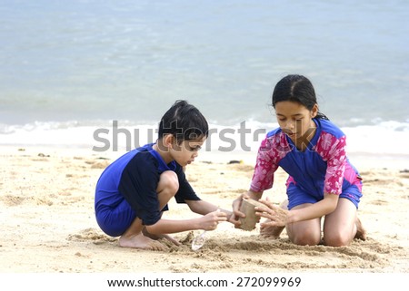 Young girl playing in the sand at the beach with younger brother