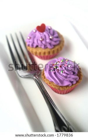 Two mini cupcakes with magenta icing and sprinkles on white plate with a fork, isolated on white