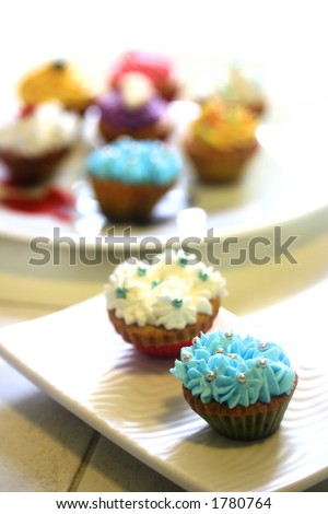 Plates of colorful mini cupcakes , isolated on white
