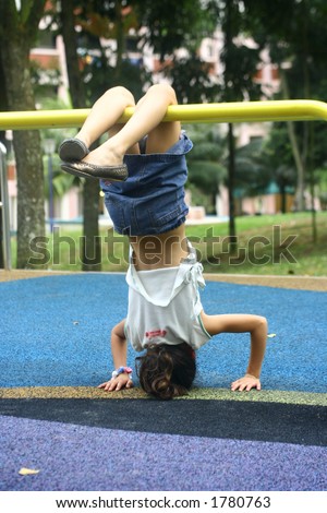 A young girl hangs upside down on a playground bar, balancing as not to fall off