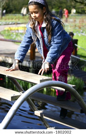 A young girl climbs on a curved steps across a river, being careful not to slip