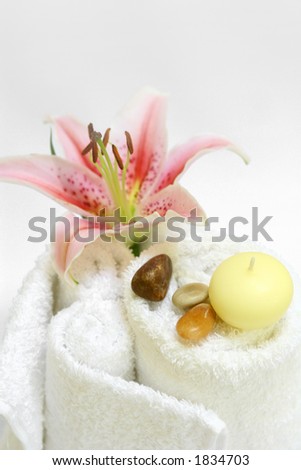 Spa setting with white towels, candles, therapy stones and a lily, on white with copy space