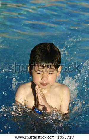 A young boy frozen in capture as he jumps into the beautiful blue water with clear drops of water splashes all around