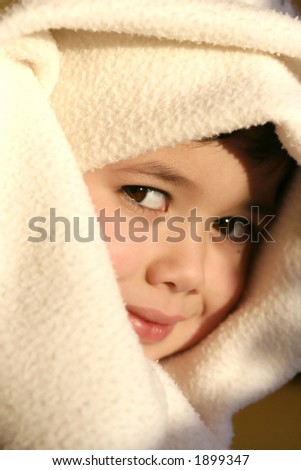 Young toddler boy plays imaginary games with his blanket,  lit by the evening glow of the sun.