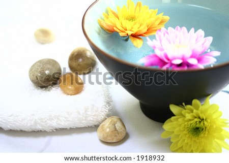 Spa / Health farm setting. White towels with a bowl of scented floral water and therapy stones on white.