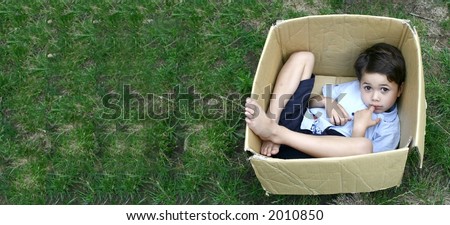 A young boy plays hide and seek in a cardboard box, with copyspace