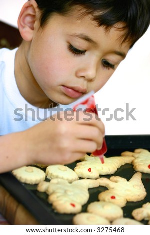 A boy squeezing red jelly coloring on his dinosaur cookies, isolated on white.