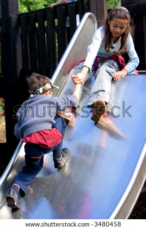 Young girl helps her brother by pulling him up to the top of the slide.