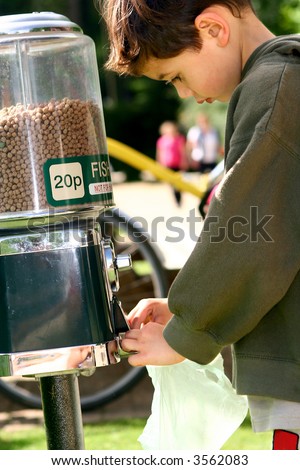 Young boy collecting some fish food from fish food dispenser, outdoors.
