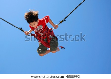 Young boy attached to jumping rope on trampoline.